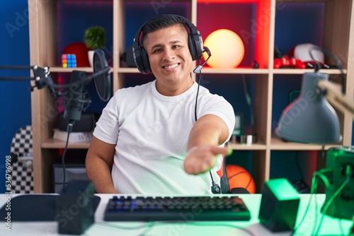 Young hispanic man playing video games smiling cheerful offering palm hand giving assistance and acceptance.