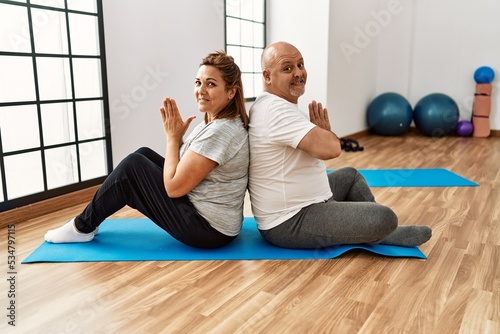 Middle age hispanic couple training yoga at sport center.