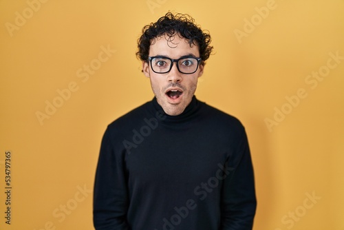 Hispanic man standing over yellow background afraid and shocked with surprise and amazed expression, fear and excited face.