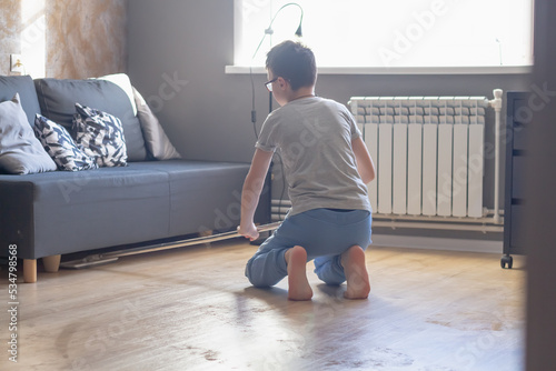 A teenage boy cleans the floor with a mop in the room, a teenage Caucasian schoolboy cleans his house