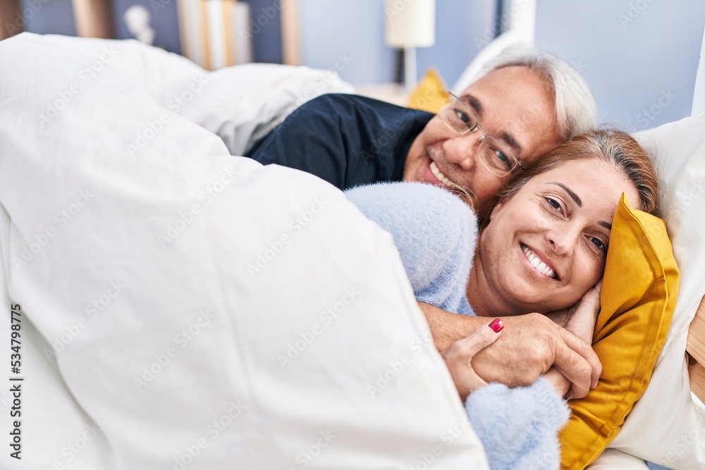 Middle age man and woman couple hugging each other lying on bed at bedroom Middle age man and woman couple hugging each other lying on bed at bedroom