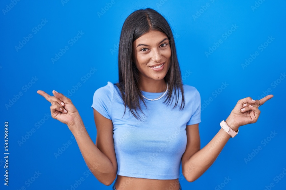 Brunette young woman standing over blue background smiling confident pointing with fingers to different directions. copy space for advertisement Brunette young woman standing over blue background smiling confident pointing with fingers to different directions. copy space for advertisement