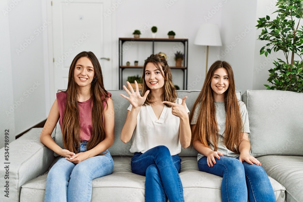 Group of three hispanic girls sitting on the sofa at home showing and pointing up with fingers number seven while smiling confident and happy. Group of three hispanic girls sitting on the sofa at home showing and pointing up with fingers number seven while smiling confident and happy.