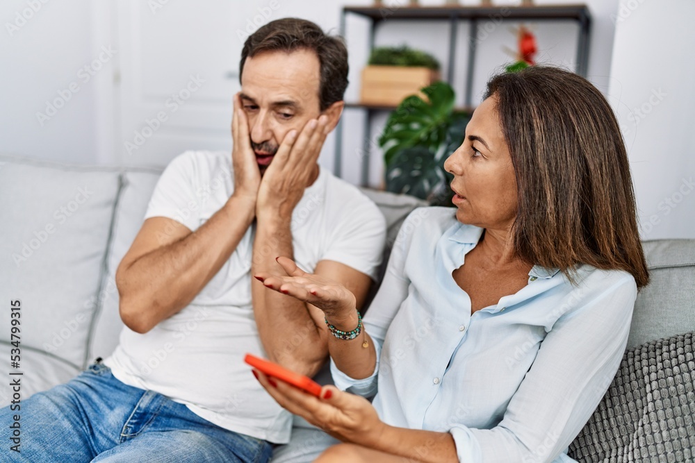 Middle age man and woman couple with problem for infidelity using smartphone at home Middle age man and woman couple with problem for infidelity using smartphone at home