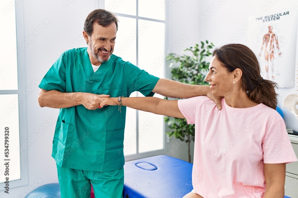 Middle age man and woman smiling confident stretching arm having rehab session at physiotherapy clinic Middle age man and woman smiling confident stretching arm having rehab session at physiotherapy clinic