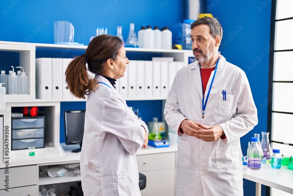Middle age man and woman scientists having conversation at laboratory Middle age man and woman scientists having conversation at laboratory