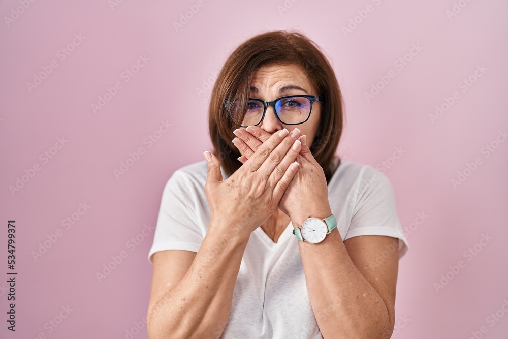 Middle age hispanic woman standing over pink background shocked covering mouth with hands for mistake. secret concept. Middle age hispanic woman standing over pink background shocked covering mouth with hands for mistake. secret concept.