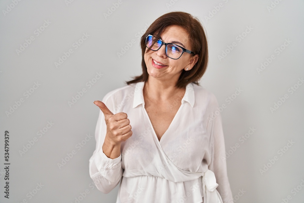 Middle age hispanic woman standing over isolated background doing happy thumbs up gesture with hand. approving expression looking at the camera showing success.
