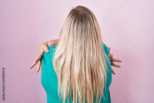 Caucasian plus size woman standing over pink background hugging oneself happy and positive from backwards. self love and self care