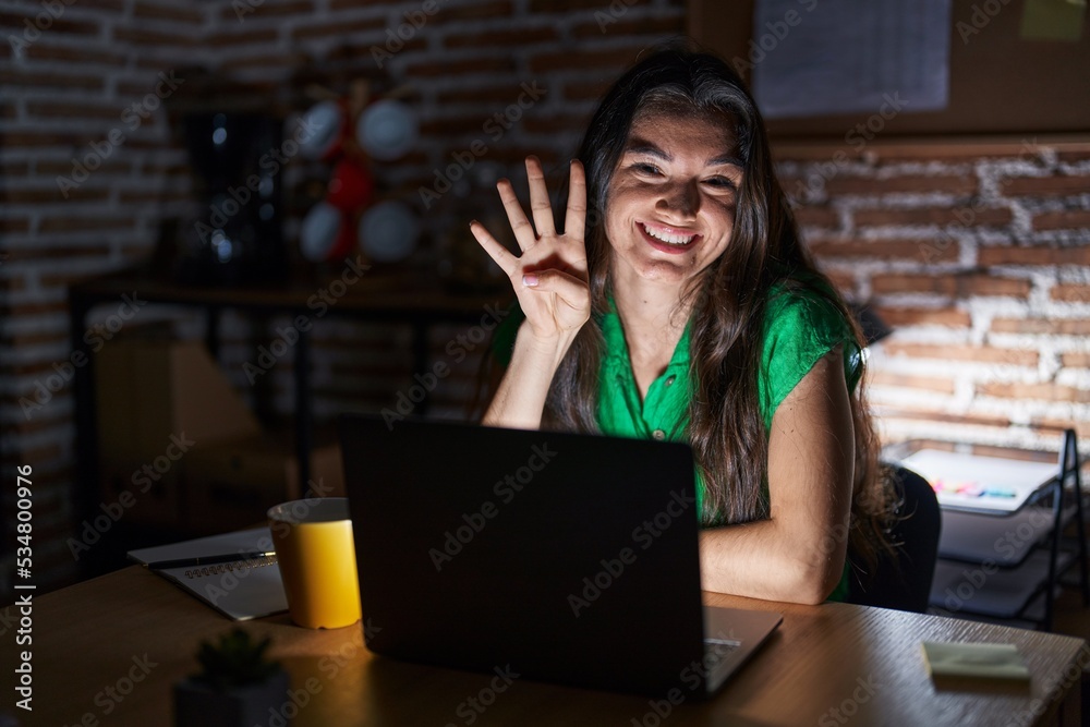Young teenager girl working at the office at night showing and pointing up with fingers number four while smiling confident and happy. Young teenager girl working at the office at night showing and pointing up with fingers number four while smiling confident and happy.