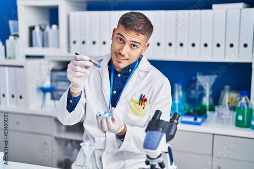 Young hispanic man scientist holding pills at laboratory