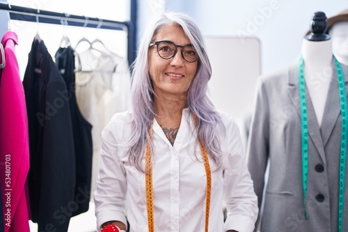 Middle age grey-haired woman tailor smiling confident standing at tailor shop photo