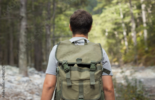 Close up hiking man from behind with his tourist backpack is walking in a forest. Healthy lifestyle concept.