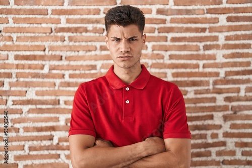 Young hispanic man standing over bricks wall skeptic and nervous, disapproving expression on face with crossed arms. negative person.