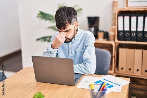 Young hispanic man business worker stressed using laptop working at office photo