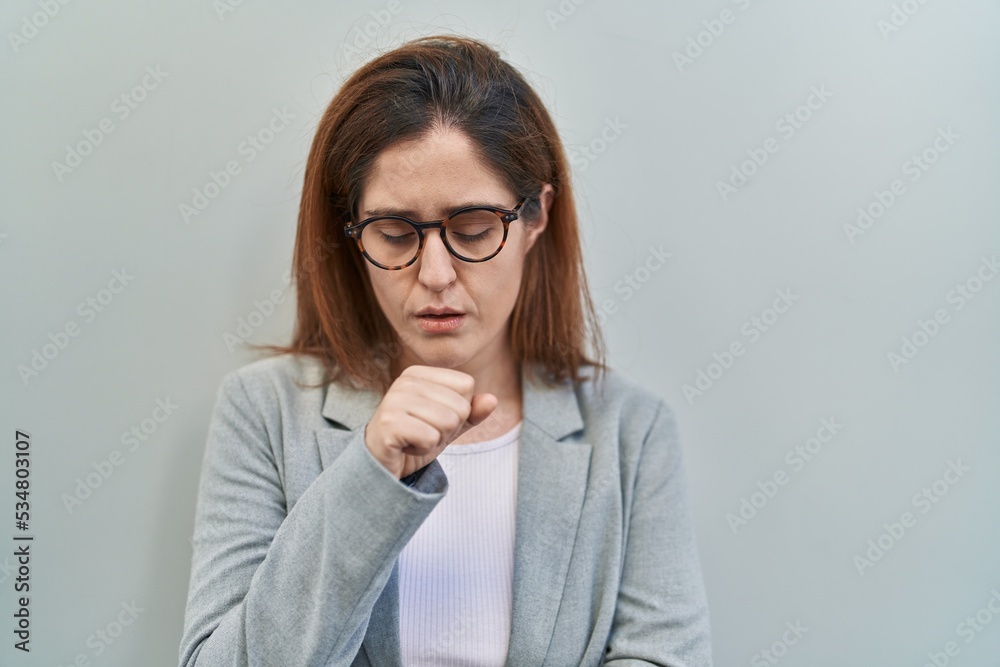 Brunette woman standing over grey background feeling unwell and coughing as symptom for cold or bronchitis. health care concept.