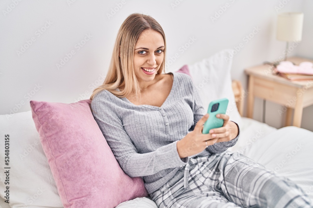 Young woman using smartphone sitting on bed at bedroom Young woman using smartphone sitting on bed at bedroom
