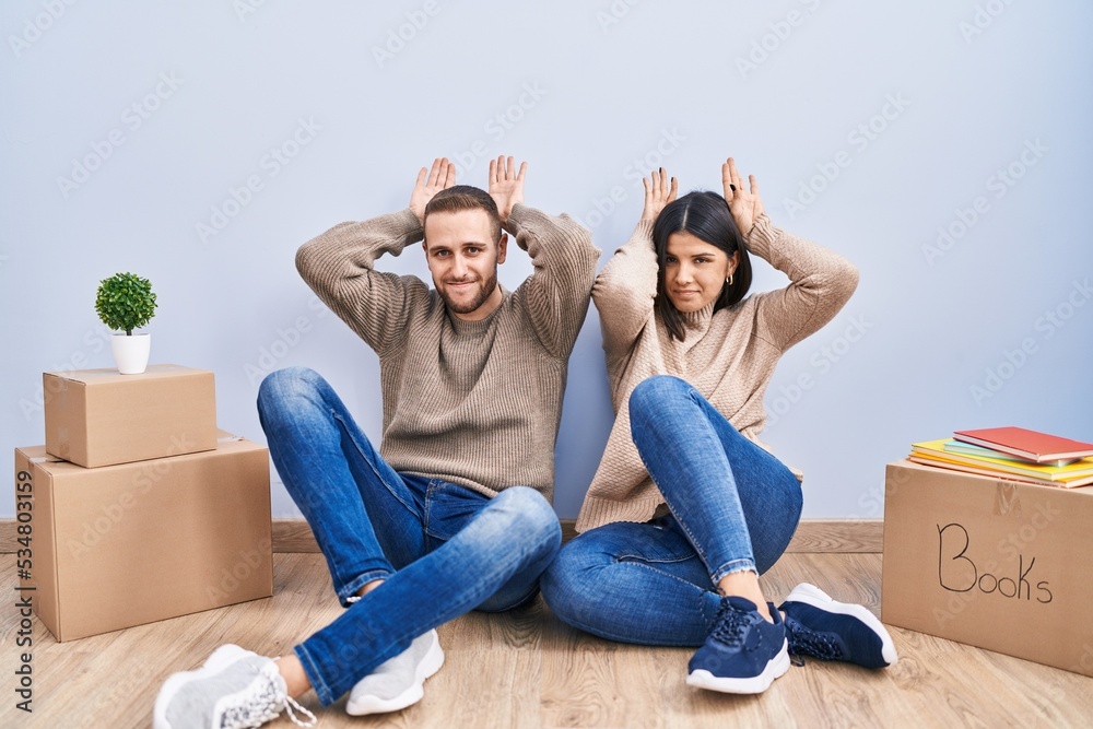 Young couple moving to a new home doing bunny ears gesture with hands palms looking cynical and skeptical. easter rabbit concept.