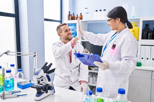 Man and woman wearing scientists uniform high five with hands raised up at laboratory