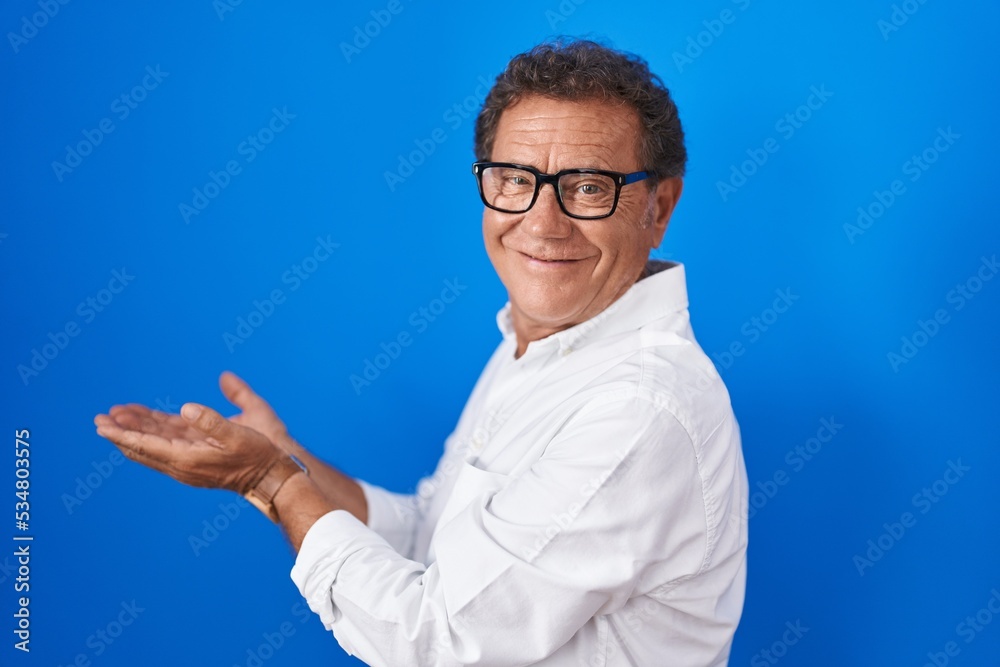 Middle age hispanic man standing over blue background pointing aside with hands open palms showing copy space, presenting advertisement smiling excited happy Middle age hispanic man standing over blue background pointing aside with hands open palms showing copy space, presenting advertisement smiling excited happy