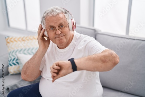 Middle age grey-haired man listening to music looking watch at home