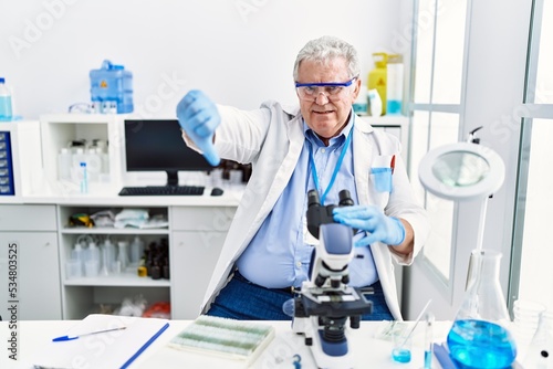 Senior caucasian man working at scientist laboratory looking unhappy and angry showing rejection and negative with thumbs down gesture. bad expression.
