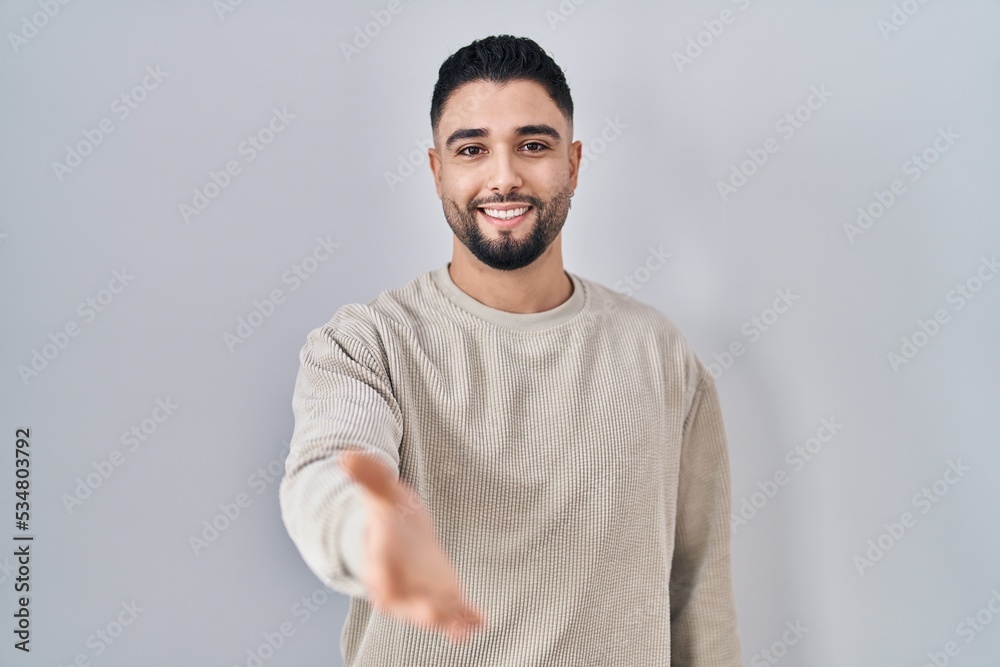 Fototapeta premium Young handsome man standing over isolated background smiling cheerful offering palm hand giving assistance and acceptance.