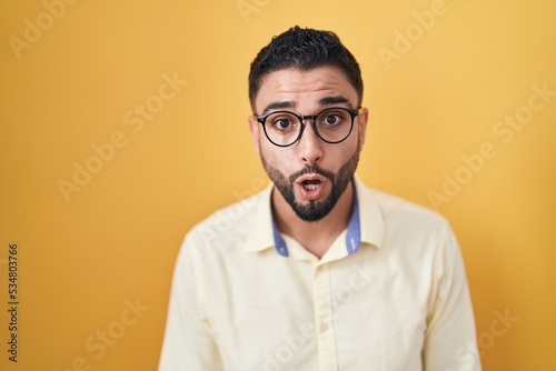 Hispanic young man wearing business clothes and glasses afraid and shocked with surprise and amazed expression, fear and excited face.
