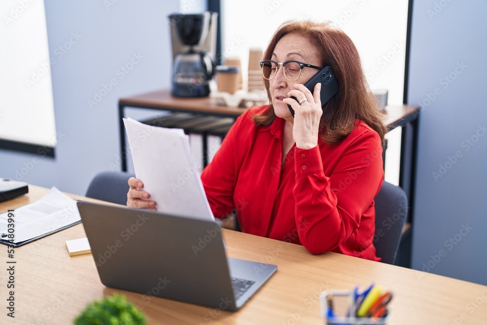 Senior woman business worker talking on smartphone reading document at office