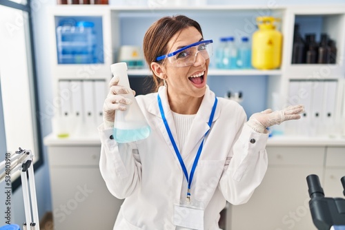 Young brunette woman working at scientist laboratory celebrating achievement with happy smile and winner expression with raised hand