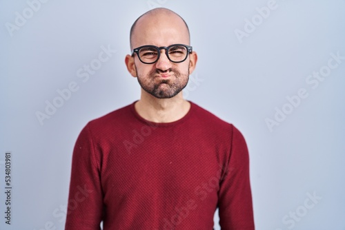 Young bald man with beard standing over white background wearing glasses puffing cheeks with funny face. mouth inflated with air, crazy expression. © Krakenimages.com