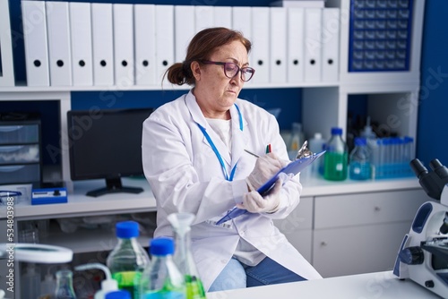 Senior woman scientist smiling confident writing on document at laboratory