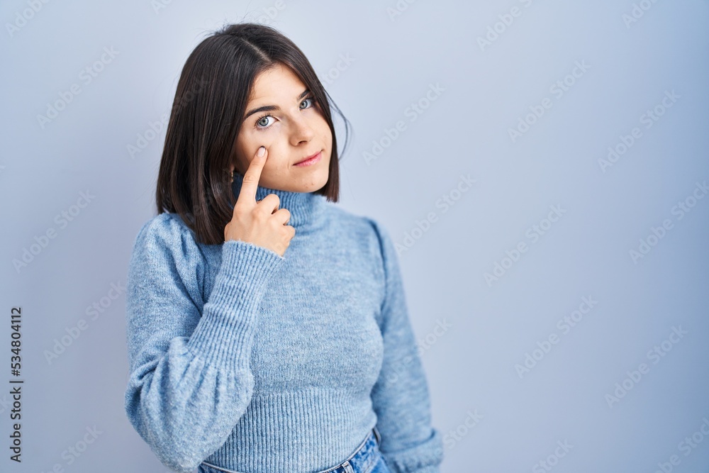 Young hispanic woman standing over blue background pointing to the eye watching you gesture, suspicious expression Young hispanic woman standing over blue background pointing to the eye watching you gesture, suspicious expression