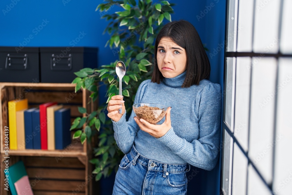 Fototapeta premium Young hispanic woman eating healthy whole grain cereals with spoon depressed and worry for distress, crying angry and afraid. sad expression.