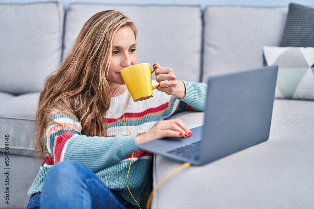 Young blonde woman using laptop drinking coffee at home Young blonde woman using laptop drinking coffee at home