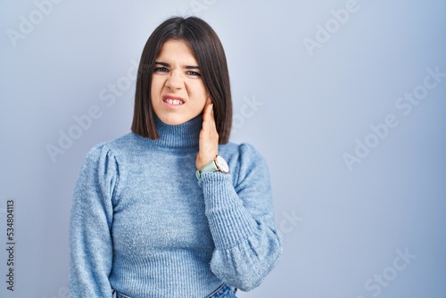 Young hispanic woman standing over blue background touching mouth with hand with painful expression because of toothache or dental illness on teeth. dentist