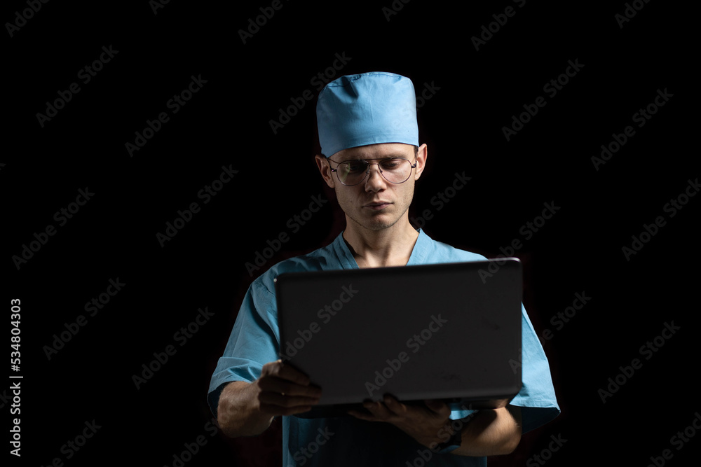 male doctor scientist speaks while looking into a laptop monitor on a dark background. The concept of online education and consultations in medicine male doctor scientist speaks while looking into a laptop monitor on a dark background. The concept of online education and consultations in medicine