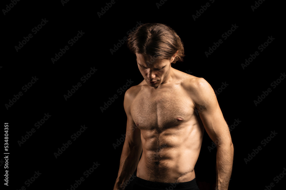 young sexy muscular man with a naked torso on a dark background. Long-haired man sportsman.