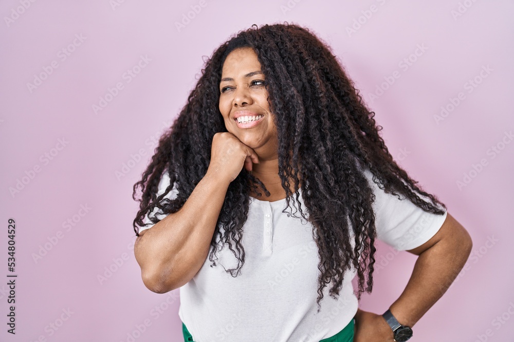 Plus size hispanic woman standing over pink background with hand on chin thinking about question, pensive expression. smiling with thoughtful face. doubt concept.