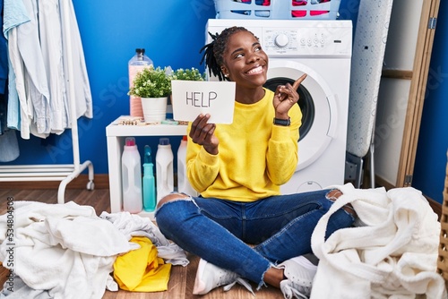 Beautiful black woman doing laundry asking for help smiling happy pointing with hand and finger to the side