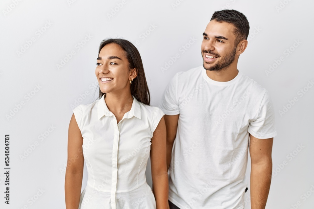 Young interracial couple standing together in love over isolated background looking away to side with smile on face, natural expression. laughing confident. Young interracial couple standing together in love over isolated background looking away to side with smile on face, natural expression. laughing confident.