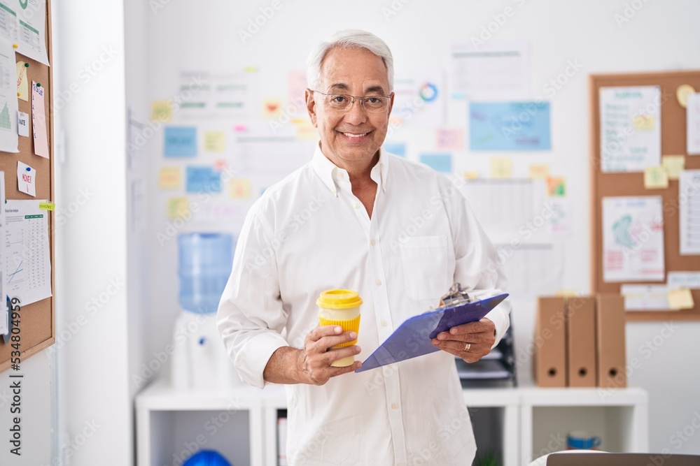 Middle age grey-haired man business worker reading document drinking coffee at office Middle age grey-haired man business worker reading document drinking coffee at office