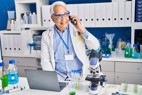 Senior man scientist using laptop talking on the smartphone at laboratory