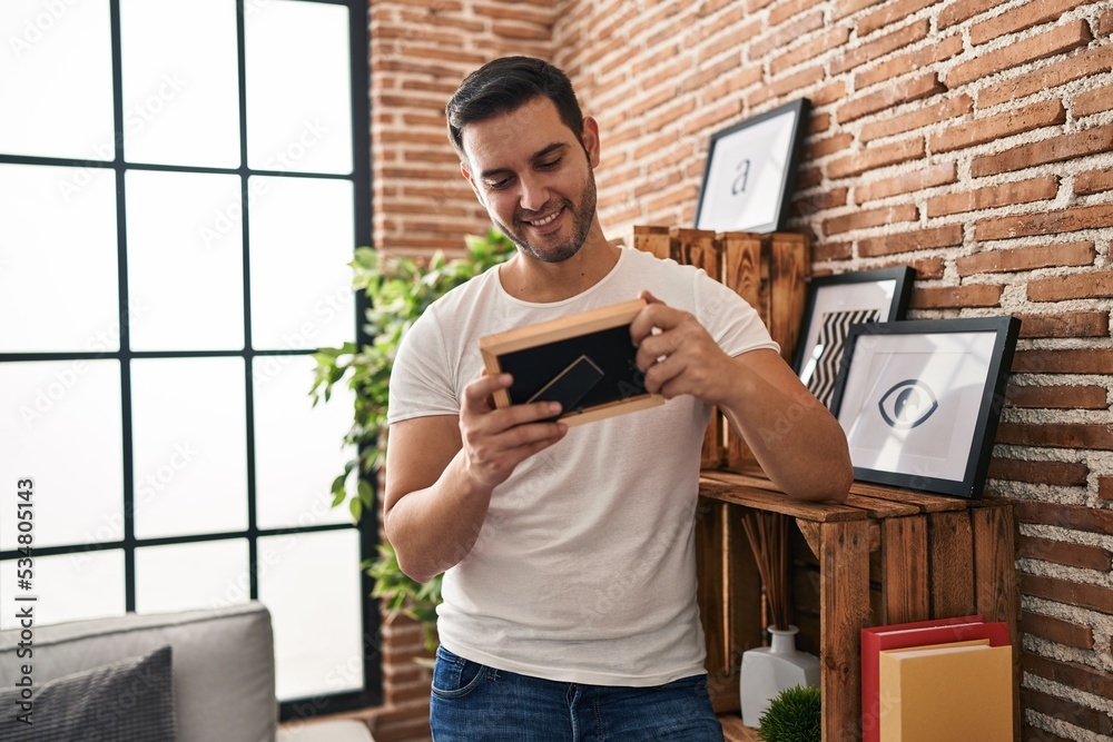 Fototapeta premium Young hispanic man looking photo standing at home