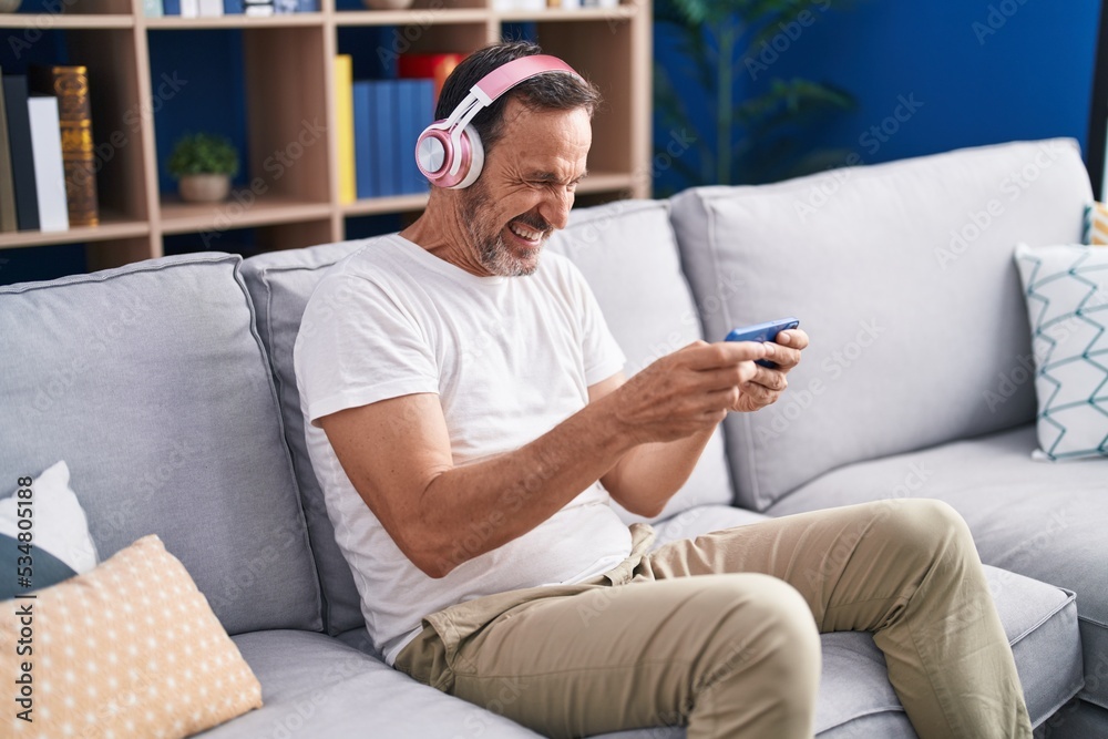 Middle age man playing video game sitting on sofa at home