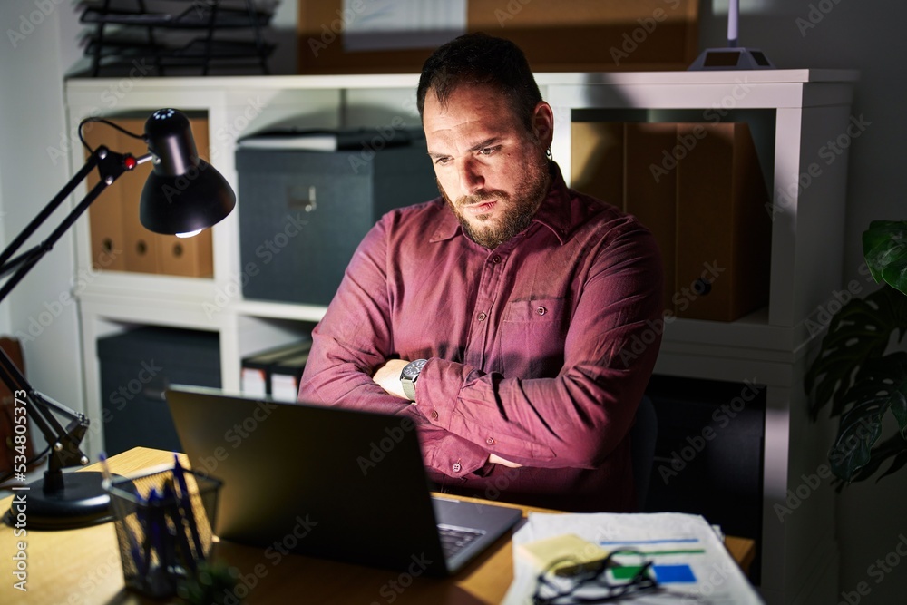 Plus size hispanic man with beard working at the office at night skeptic and nervous, disapproving expression on face with crossed arms. negative person. Plus size hispanic man with beard working at the office at night skeptic and nervous, disapproving expression on face with crossed arms. negative person.