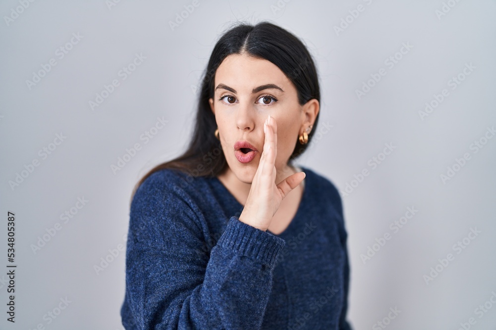 Young brunette woman standing over isolated background hand on mouth telling secret rumor, whispering malicious talk conversation Young brunette woman standing over isolated background hand on mouth telling secret rumor, whispering malicious talk conversation