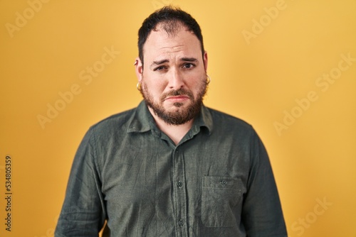 Plus size hispanic man with beard standing over yellow background depressed and worry for distress, crying angry and afraid. sad expression.