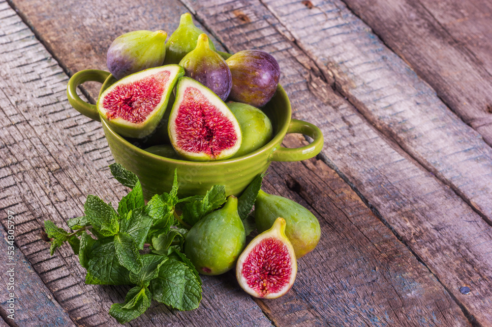 Ripe sweet figs in a green bowl on a wooden table. Figs copy space