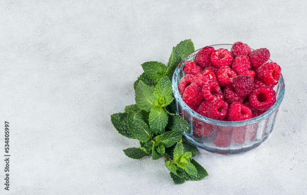 Bowl of fresh juicy raspberries on a gray background. Raspberry and mint copy space